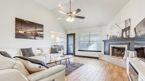 Un salon spacieux doté d’une cheminée, d’un ventilateur de plafond et de grandes fenêtres.