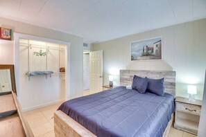 A bedroom with a large bed, a wooden headboard, a nightstand with a lamp, a painting on the wall, and a door leading to another room. - Patio & Grill: Idyllic Sorrento Vacation Home! (Sorrento)