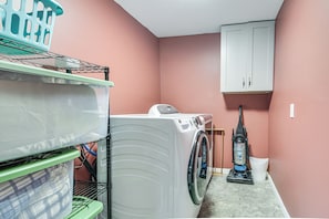 A laundry area with a washing machine, a vacuum cleaner, and storage shelves. - Fireside Winter Escape: Spacious Wilton Getaway (Wilton)