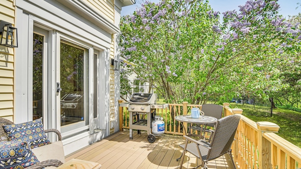 Une terrasse dotée de mobilier d’extérieur, d’un barbecue et offrant une vue sur un arbre aux fleurs violettes.