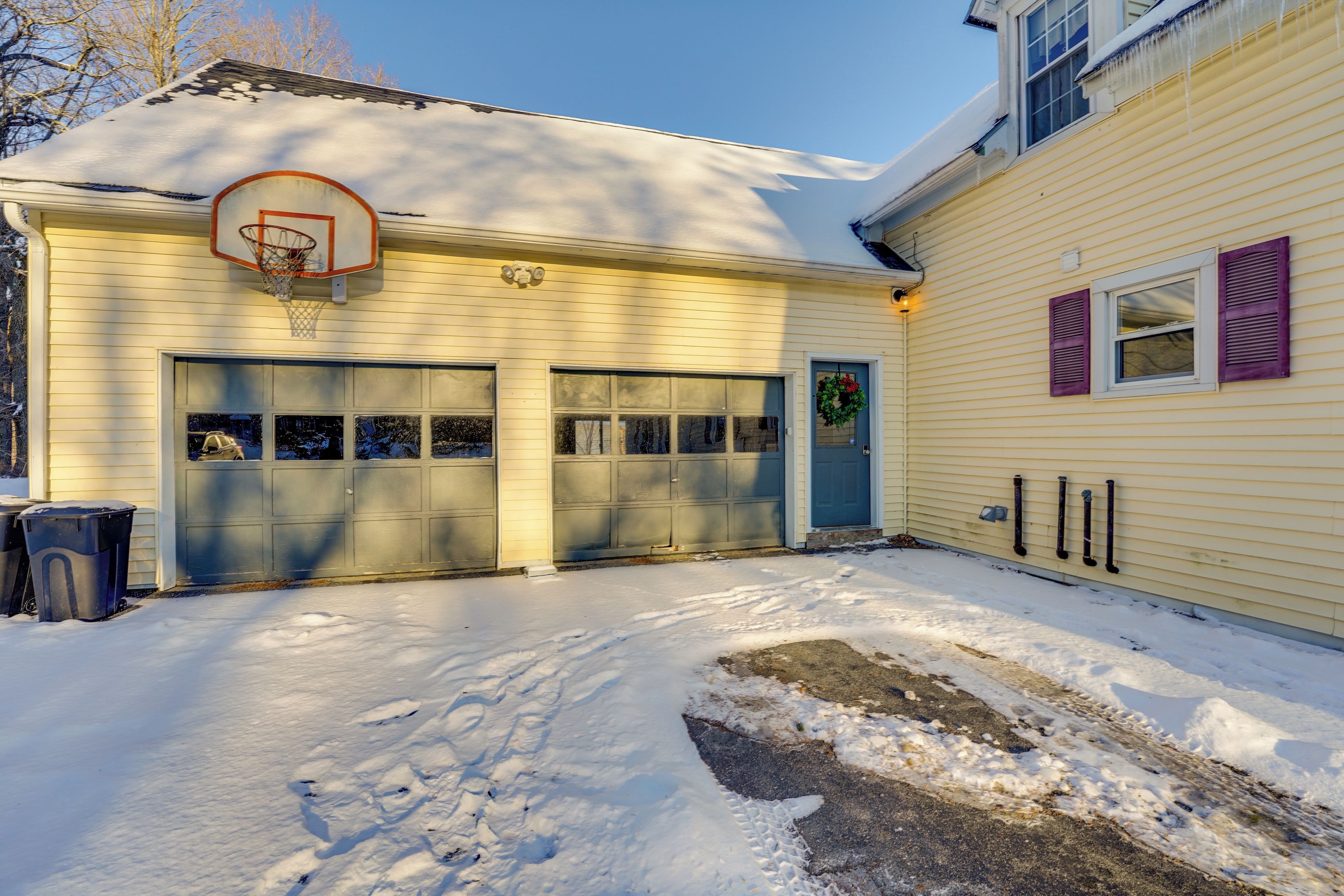 A two-story house with a garage, a basketball hoop, and a snow-covered driveway.