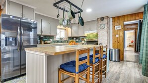 Une cuisine moderne dotée d’appareils électroménagers en acier inoxydable, d’un îlot central en bois avec des tabourets, et de casseroles suspendues.