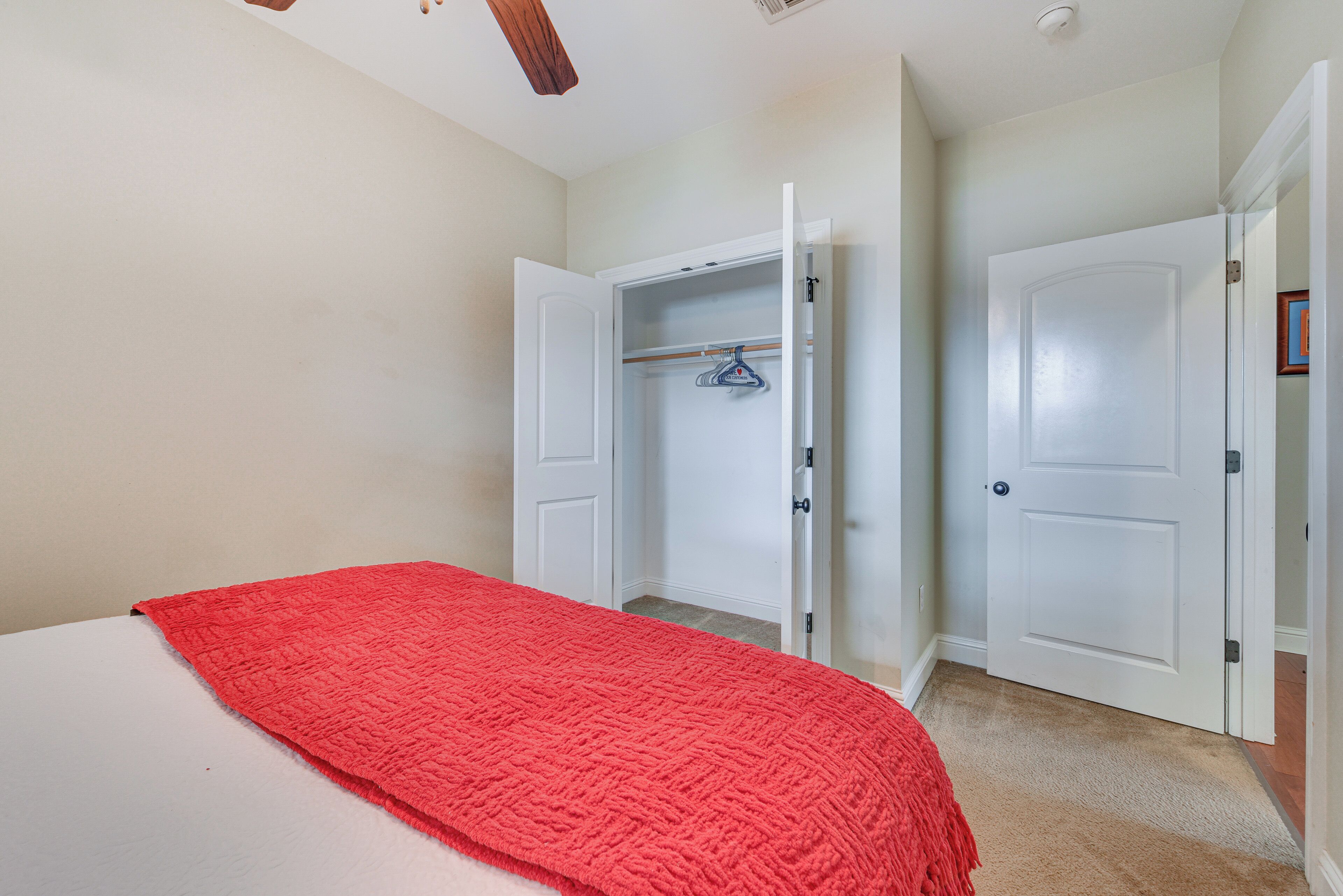 A bedroom with a bed, a red blanket, and an open closet with a hanging rack.