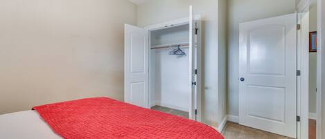 A bedroom with a bed, a red blanket, and an open closet with a hanging rack.