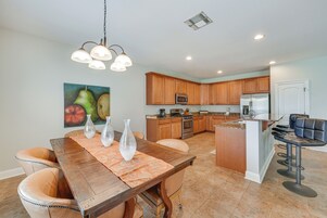 Una cocina moderna con armarios de madera, una isla central y una zona de comedor con mesa y sillas de madera.