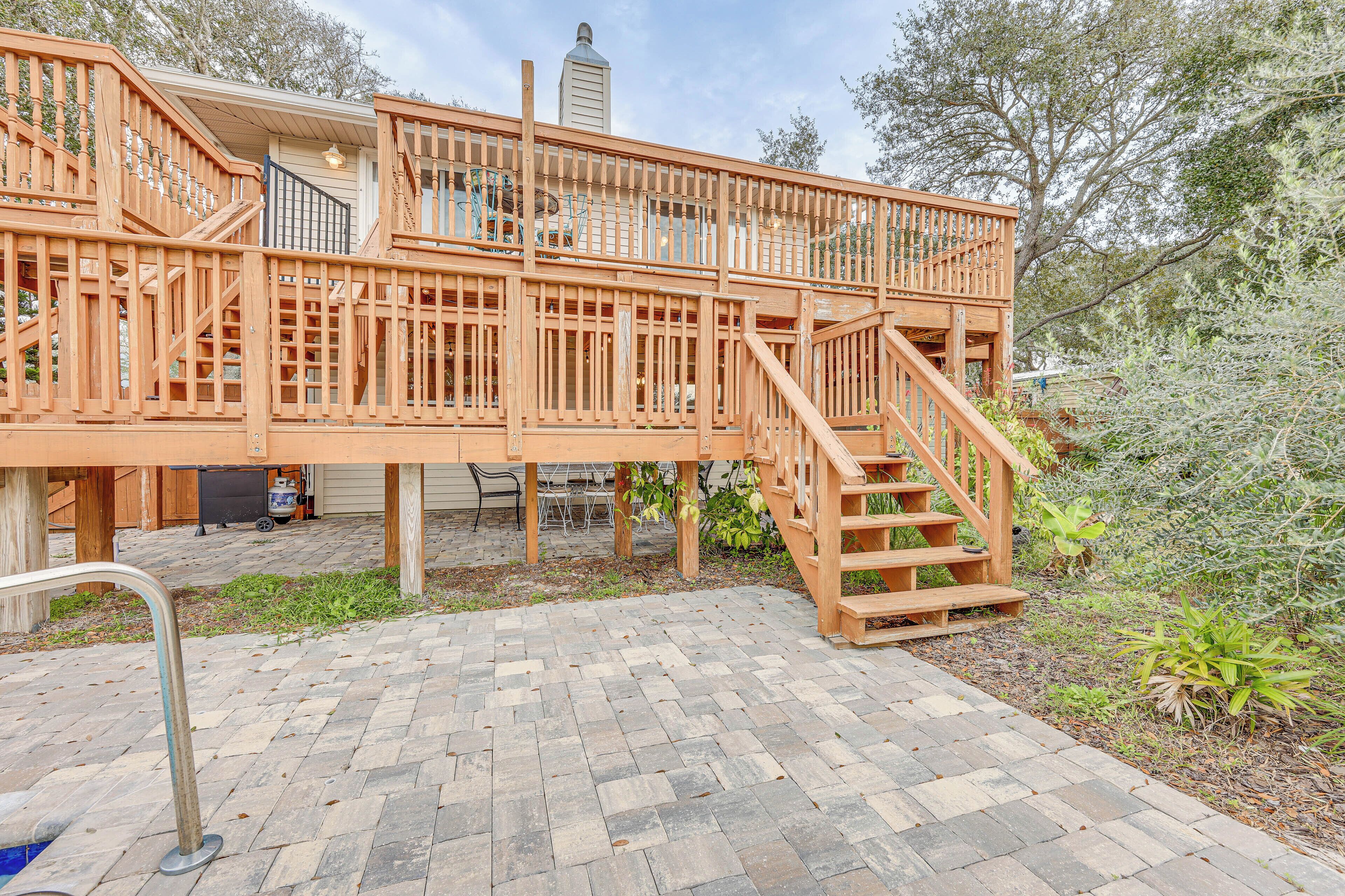 A wooden deck with a staircase, surrounded by a brick patio and greenery.