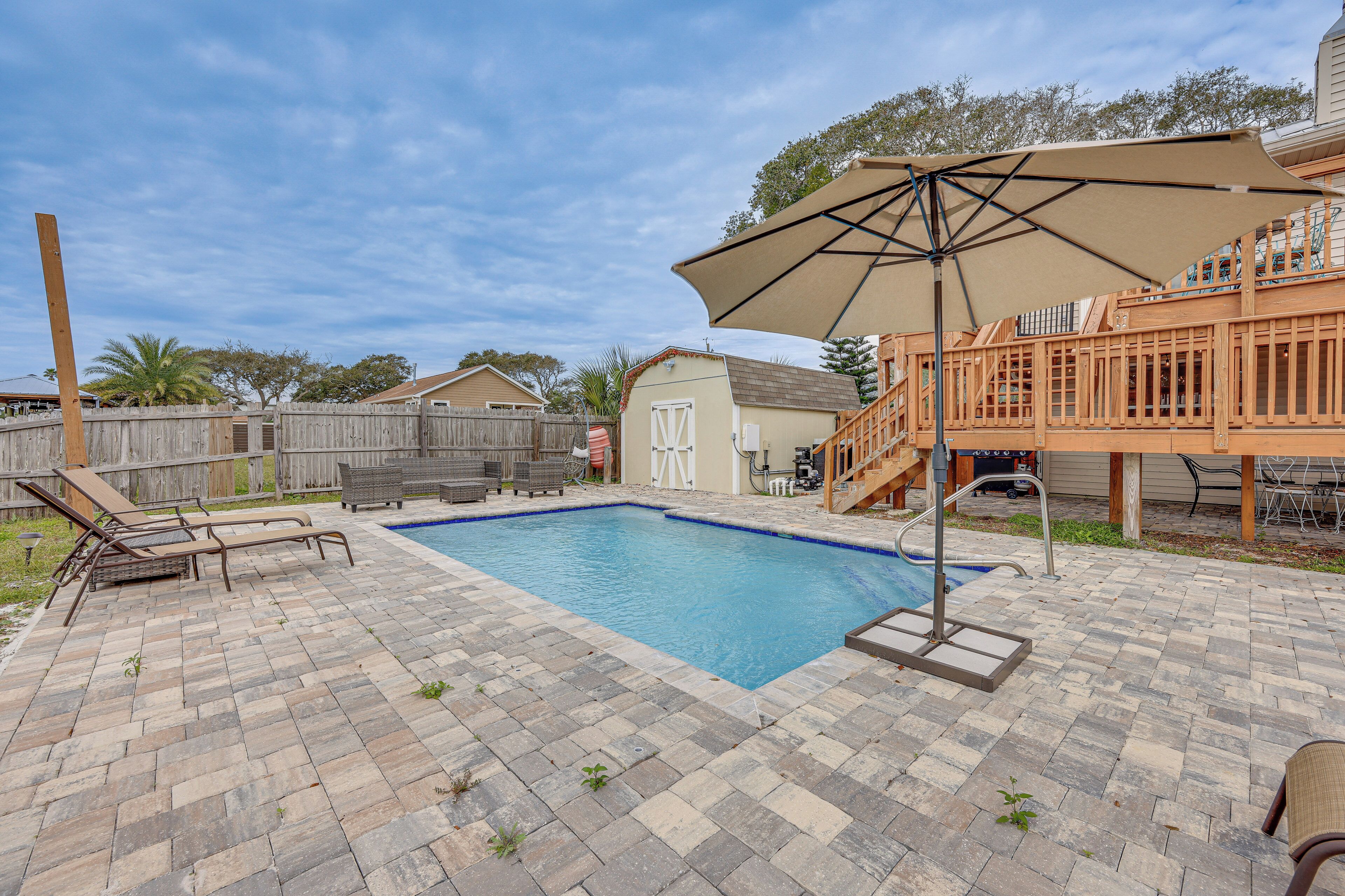 A backyard with a swimming pool, lounge chairs, a wooden deck, and a covered patio area.