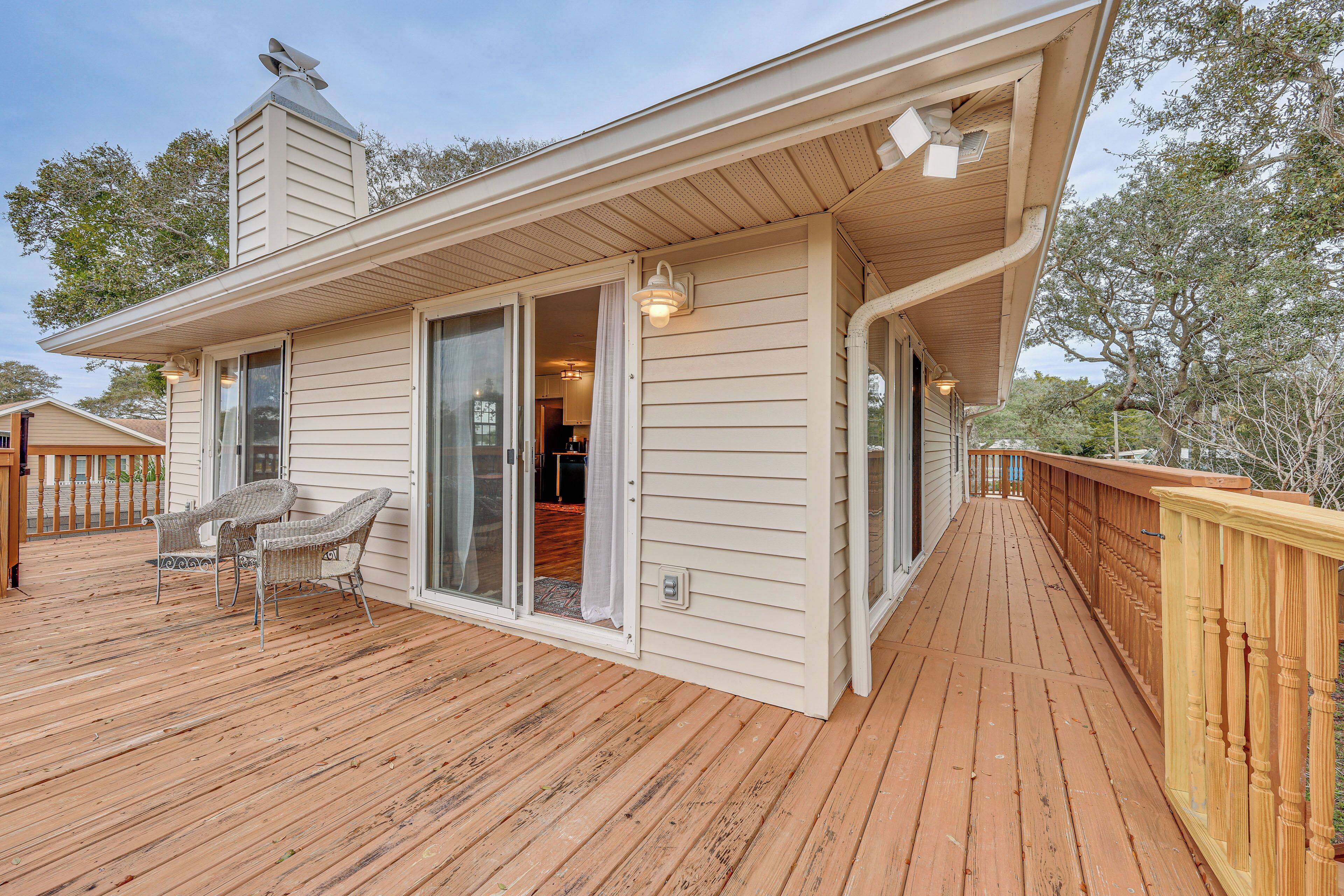 A wooden deck with wicker chairs, a covered area with sliding glass doors, and a chimney.