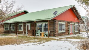 A log cabin with a green roof and red exterior, featuring a small porch with chairs and a table. - Charming Duplex w/ Patio: 12 Mi to Grand Targhee! (Driggs)