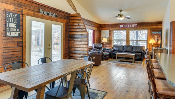 A log cabin interior with a dining area, a sofa, a fireplace, and a ski lift sign. - Charming Duplex w/ Patio: 12 Mi to Grand Targhee! (Driggs)