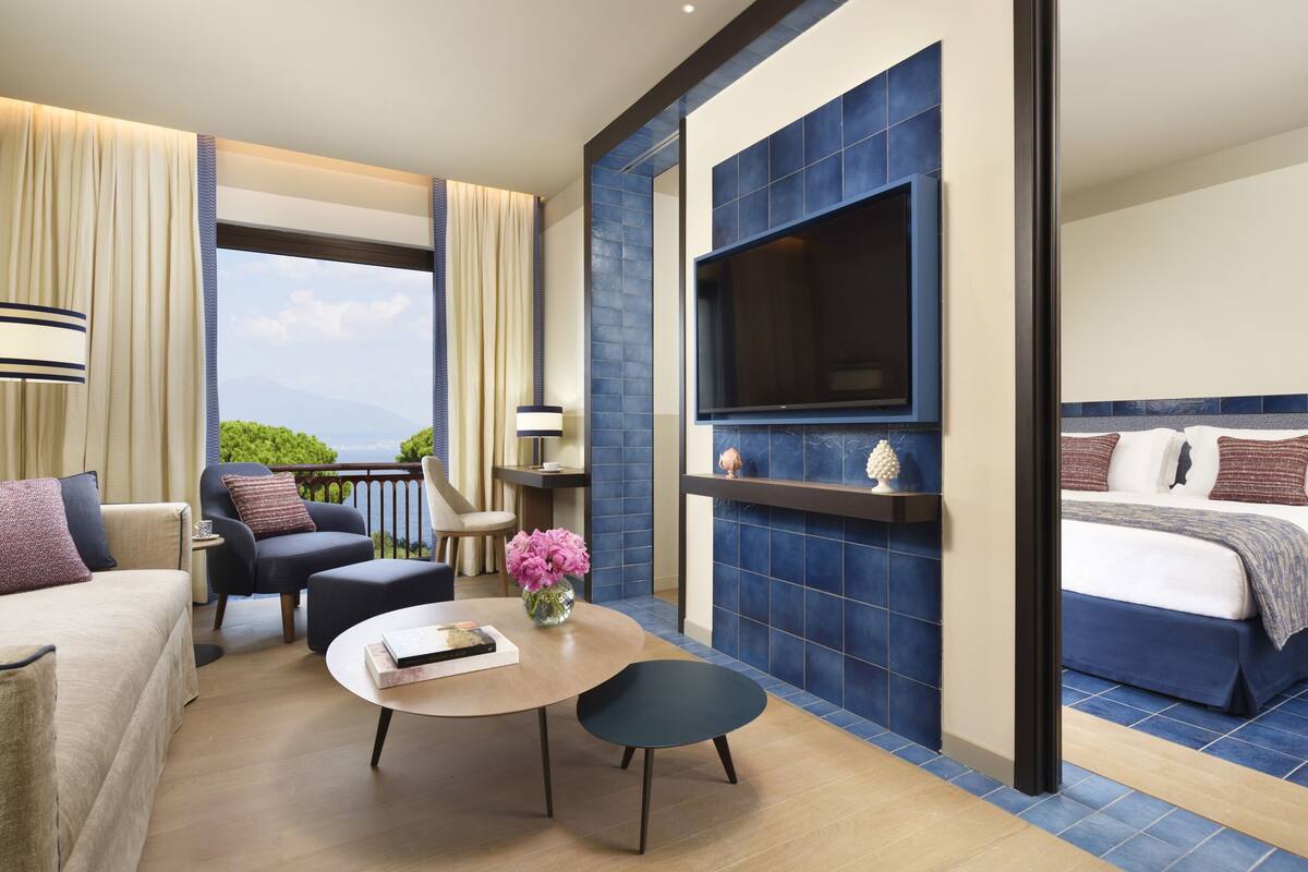 A hotel room with a bed, a TV, a seating area with a table and chairs, and a view of the outdoors.