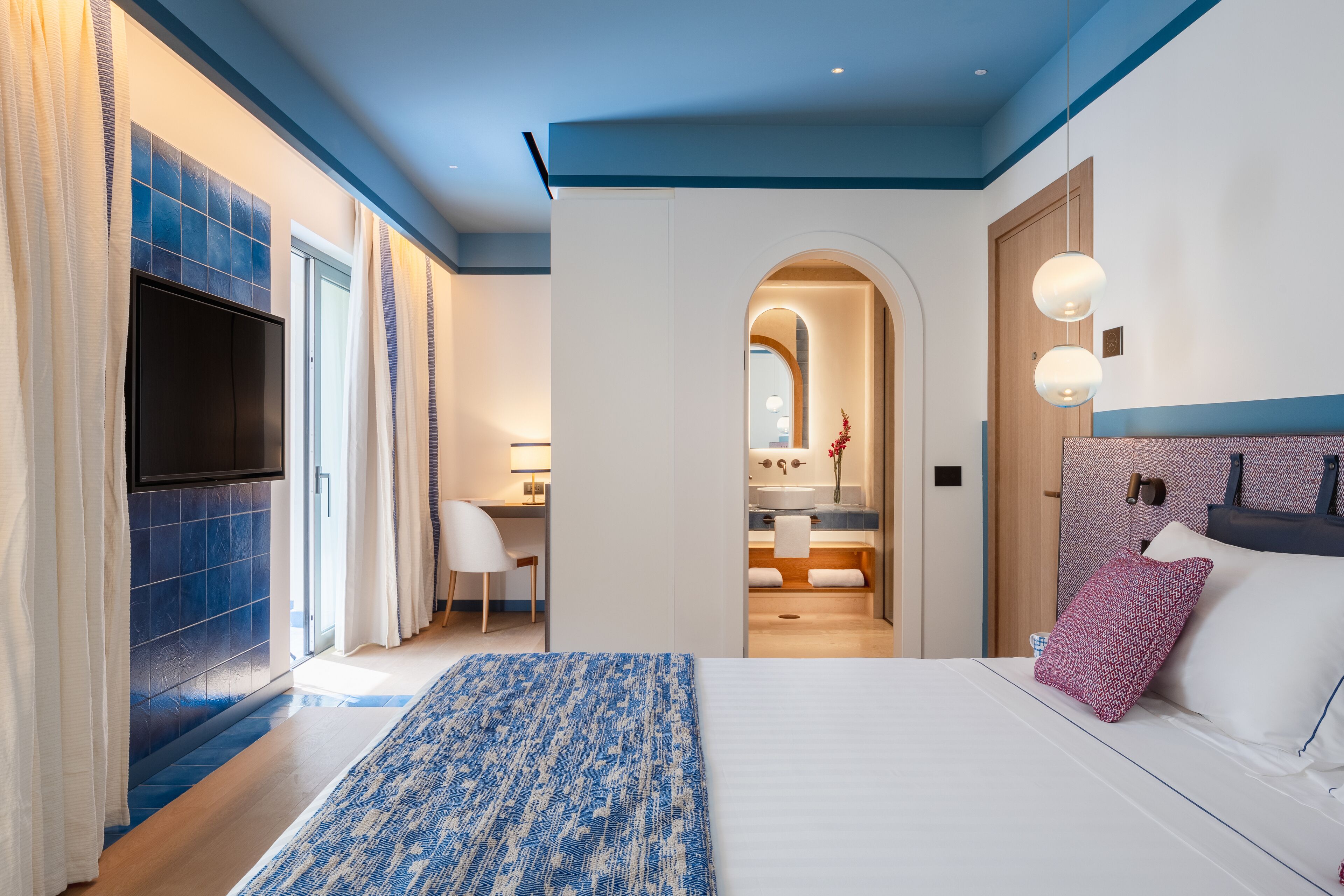 A modern hotel room with a large bed, a TV, a desk, and a bathroom.