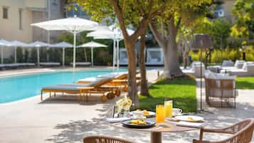 Enjoy a meal in a serene outdoor setting surrounded by lush greenery and a swimming pool.