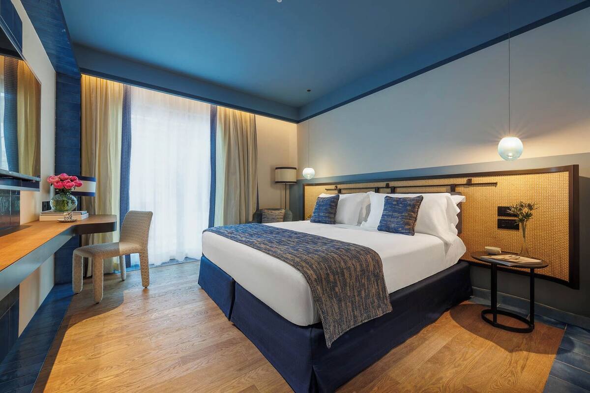 A modern hotel room with a large bed, a desk, and a chair.