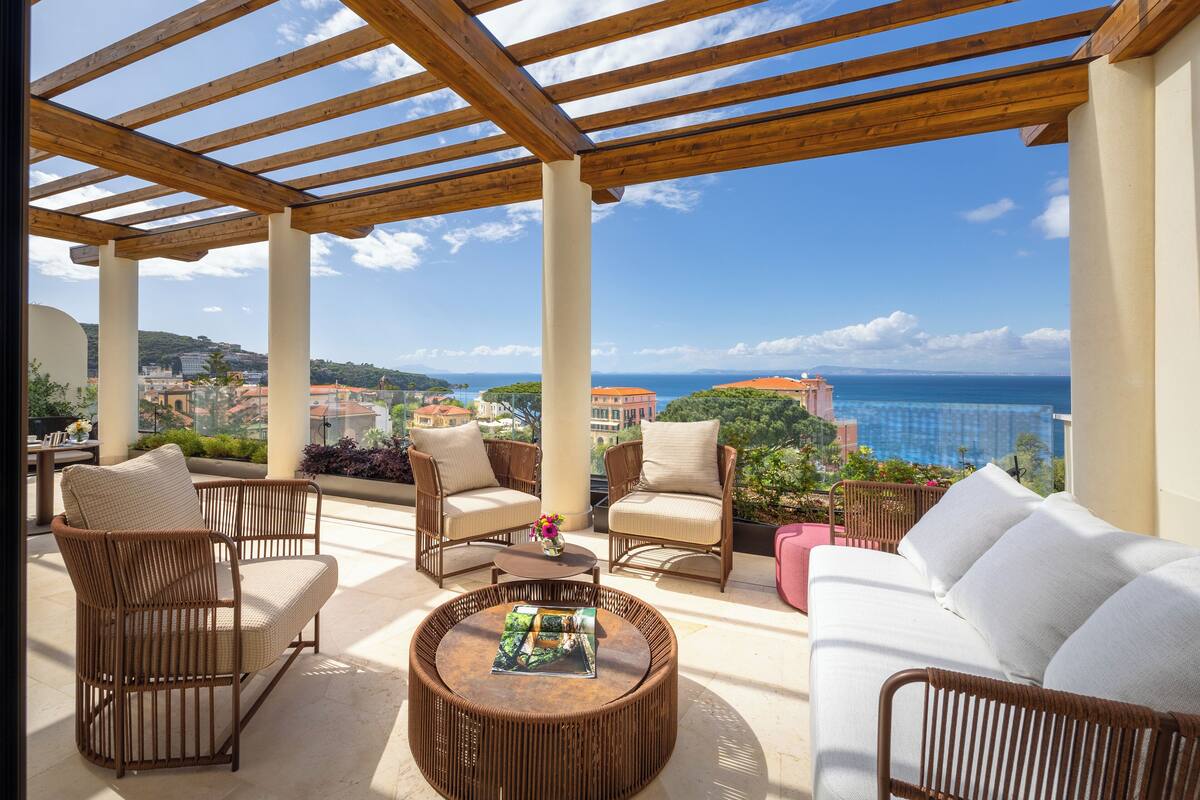 A covered outdoor seating area with wicker furniture and a view of the ocean.