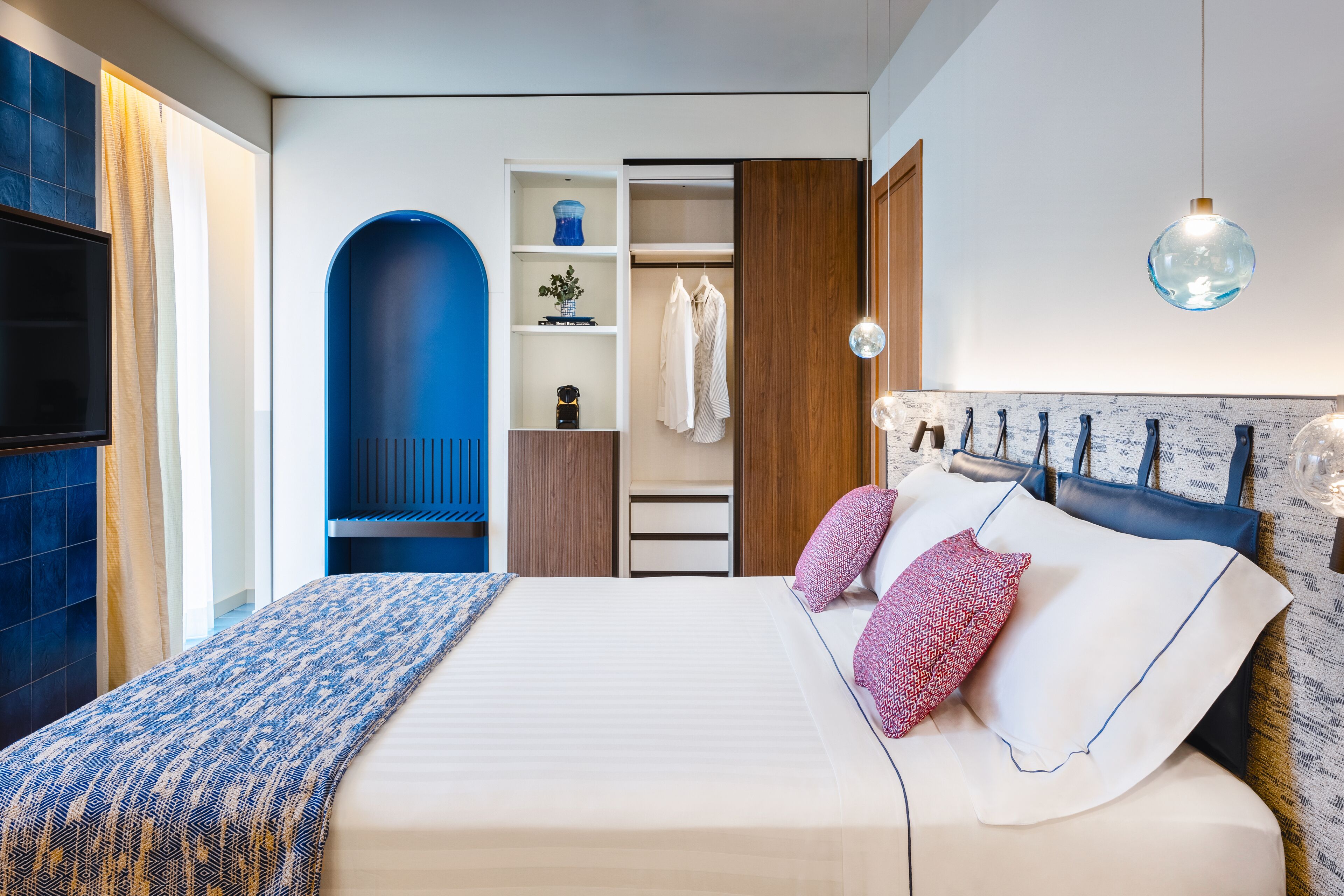 A modern bedroom with a large bed, a wardrobe, a vanity, and a hanging light fixture.