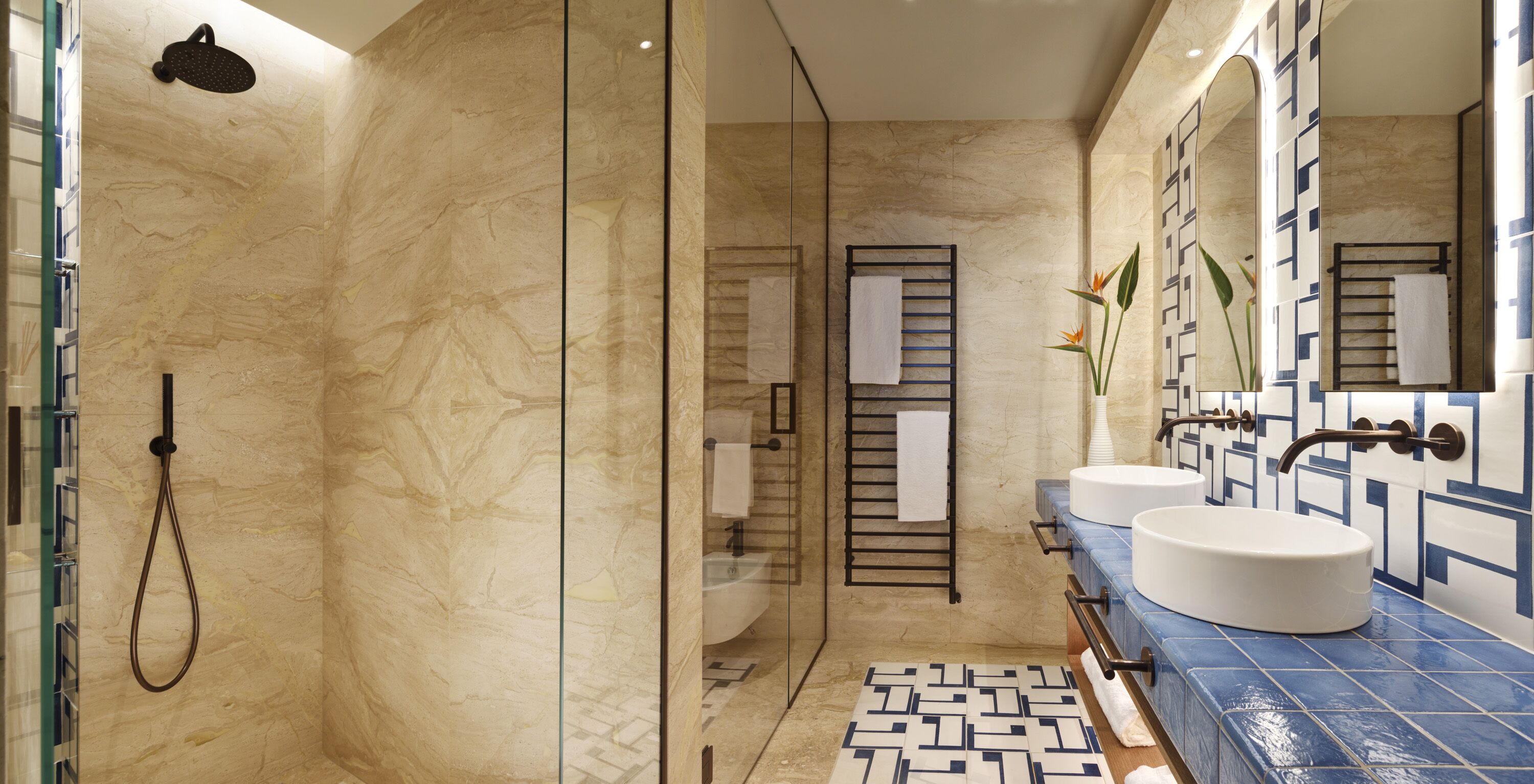 Une salle de bain moderne avec une douche à parois de verre, deux lavabos et un carrelage décoratif.