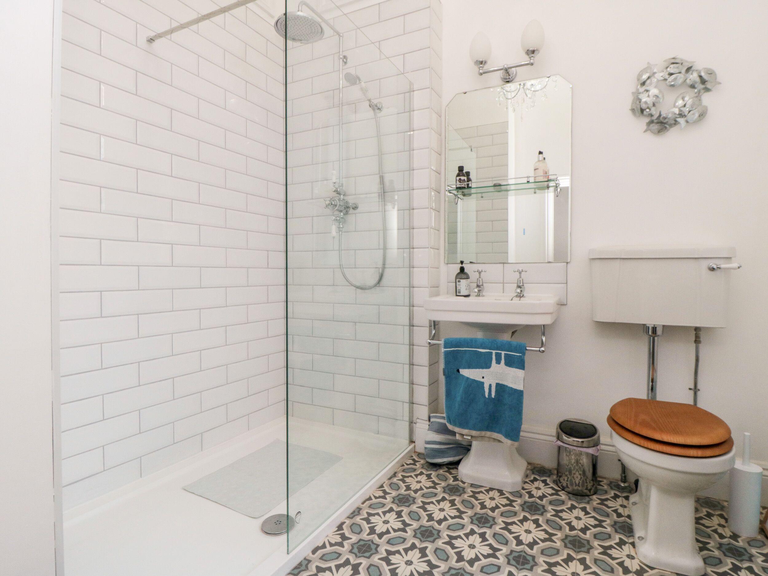 Une salle de bain avec une douche à parois de verre, un lavabo blanc avec un miroir au-dessus, et des toilettes avec un abattant en bois.