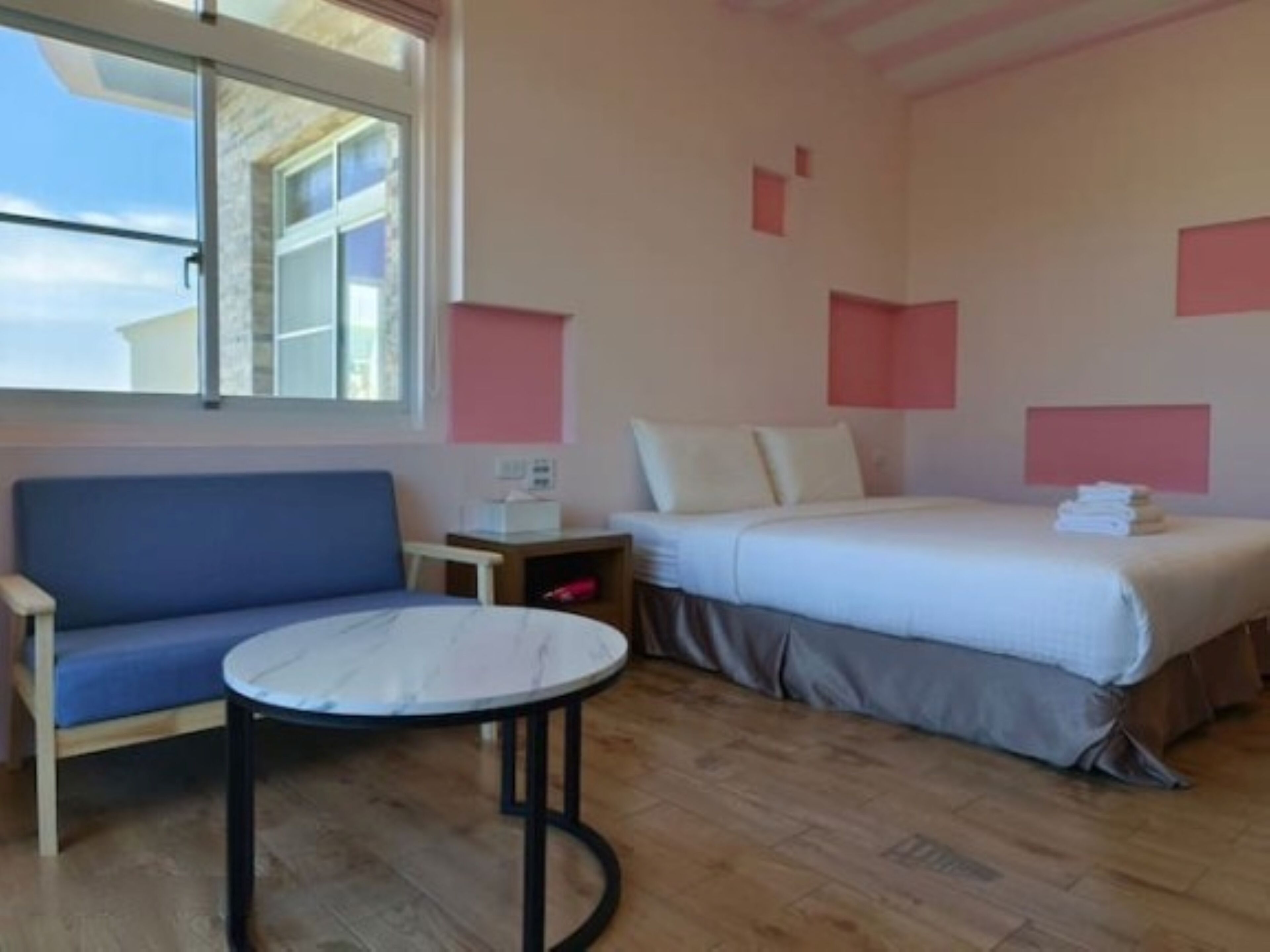 A hotel room with a bed, a blue sofa, a round table, and a window with a view of buildings.