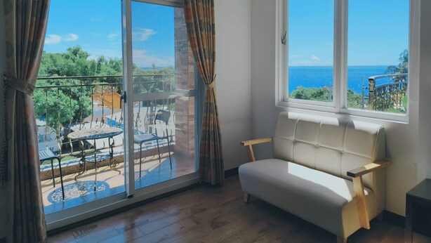 A room with a sofa and a window overlooking a balcony with outdoor furniture. - Lunar Mare inn (Liuqiu)