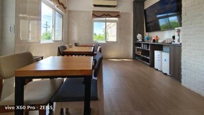 A dining area with wooden tables and chairs, a flat-screen TV mounted on a brick wall, and a kitchen area with appliances. - Lunar Mare inn (Liuqiu)