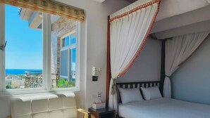A bedroom with a bed, a bedside table, a chair, and a window with a view of the sea. - Lunar Mare inn (Liuqiu)