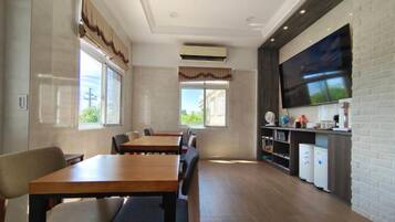 A dining area with wooden tables and chairs, a flat-screen TV mounted on a brick wall, and a kitchen area with appliances.