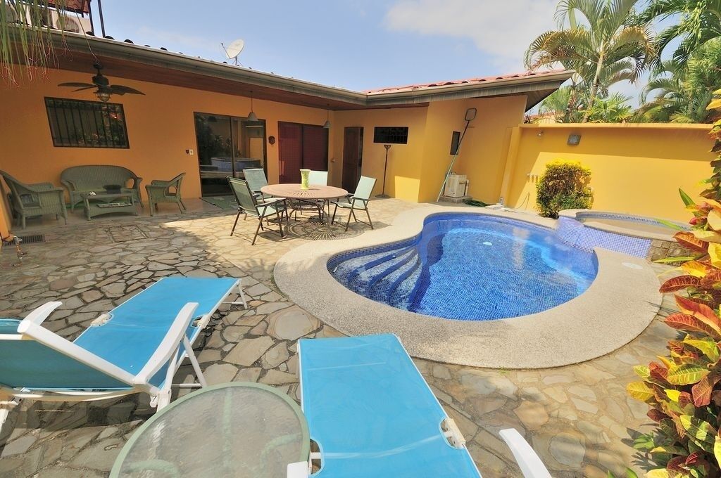 A backyard with a swimming pool, lounge chairs, a dining table, and a ceiling fan.