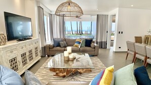 A modern living room with a large TV, a glass coffee table, and a sofa with colorful cushions.