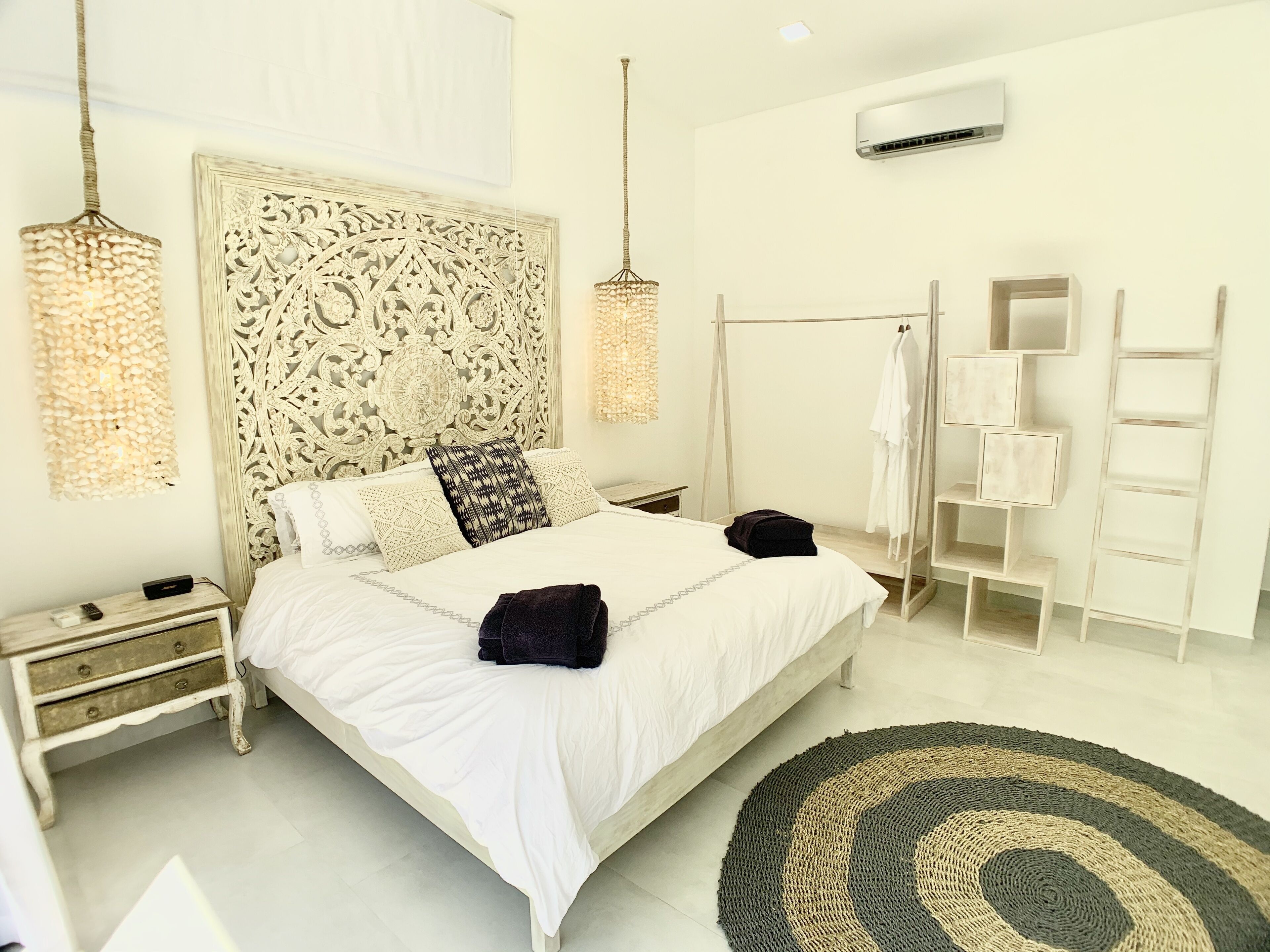 Une chambre avec un grand lit, une table de chevet, une lampe de chevet, un luminaire suspendu, une armoire et un tapis rond.