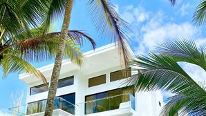 A modern multi-story house with a swimming pool, surrounded by palm trees.