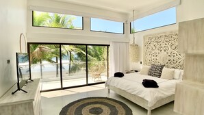 A modern bedroom with a large bed, a decorative headboard, and a view of palm trees through large windows.