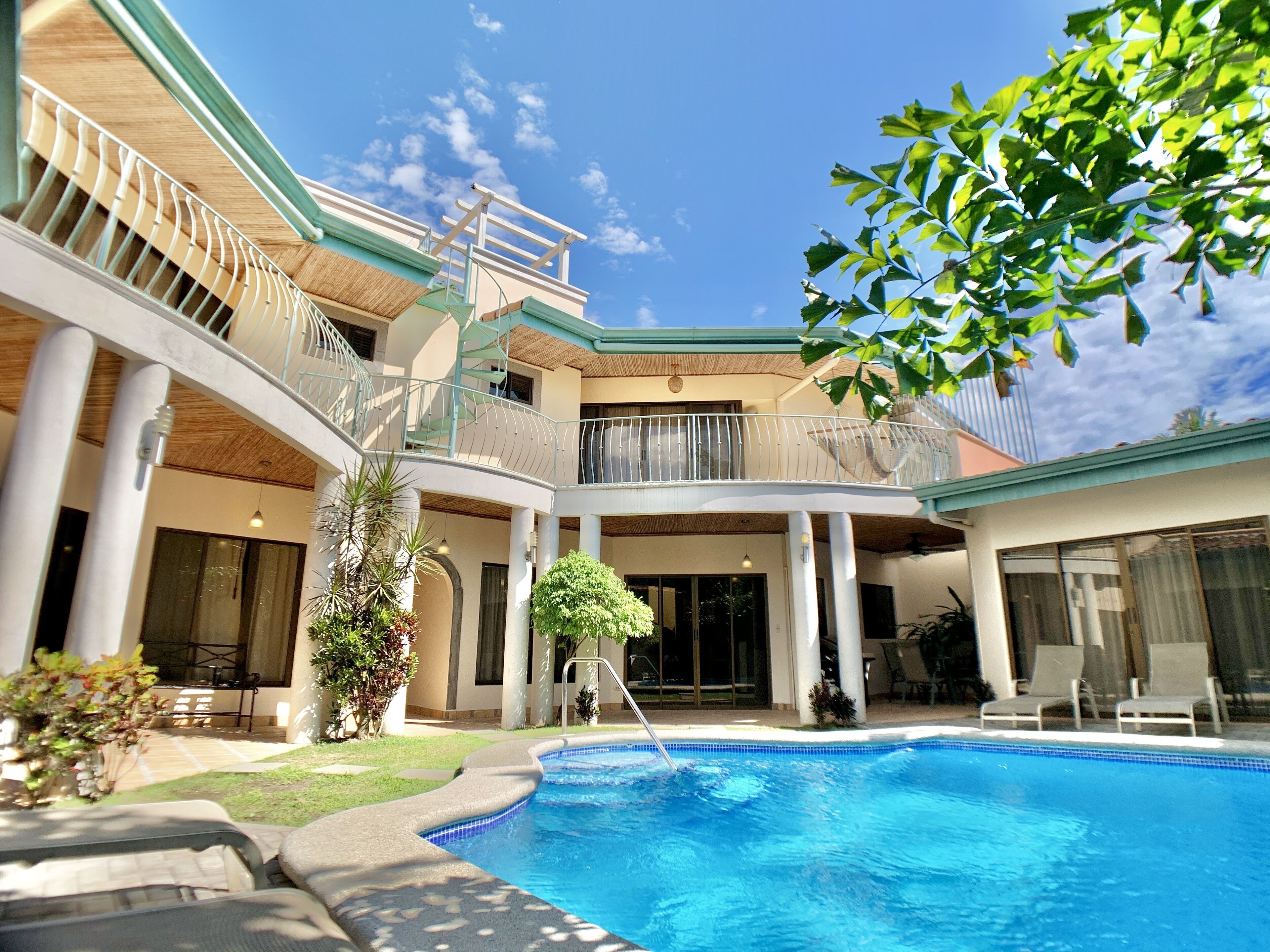 A multi-level pool area with a clear blue pool, surrounded by white columns and covered balconies.