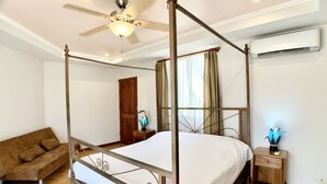 A four-poster bed with a ceiling fan, a nightstand with a lamp, a wooden door, and a brown sofa. - Villa Arenas: Private Pool & Easy Beach Access in Jaco by RedAwning (Jacó)