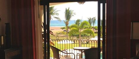 Ein Zimmer mit Bett, Blick auf Pool und Strand sowie ein Balkon mit Stühlen und Tisch.