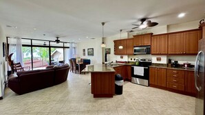 A spacious kitchen with wooden cabinets, a central island, and a dining area with a sofa and chairs. - 3 Bedroom Condo w/ Ocean View - Tres Regalos 201N by RedAwning (Jacó)