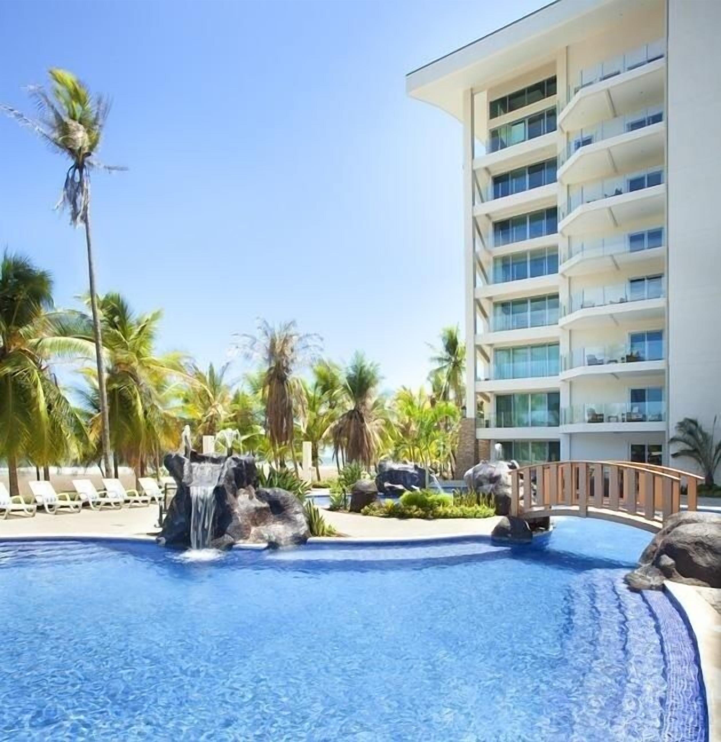Un hôtel moderne doté d’une piscine agrémentée d’une cascade et de palmiers.
