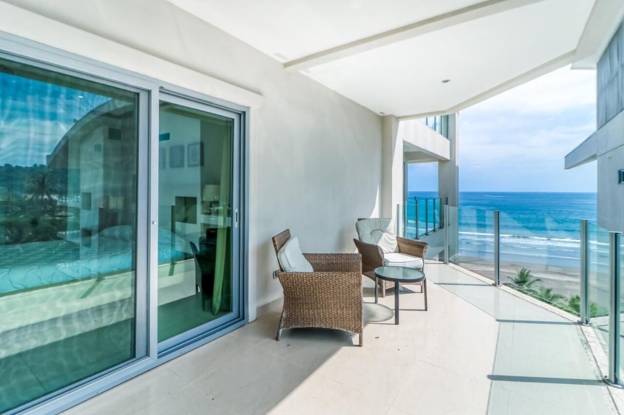 A balcony with a glass door, wicker furniture, and a view of the ocean.