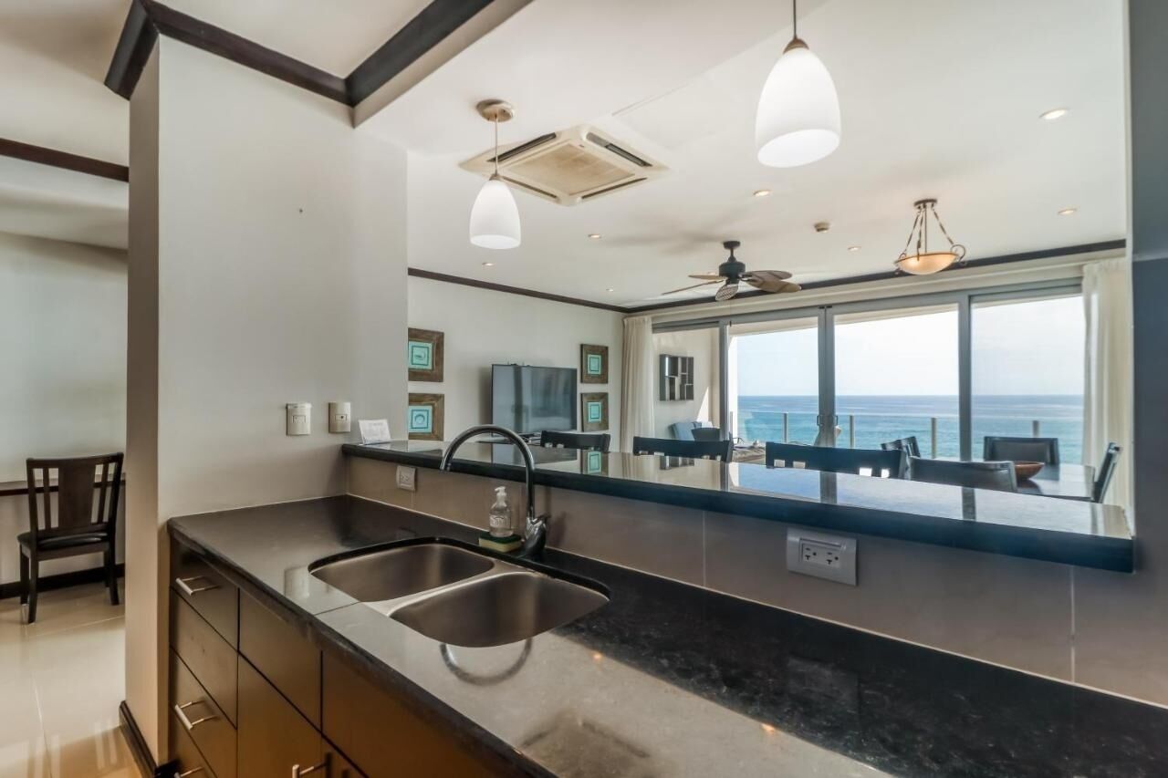 A modern kitchen with a large window overlooking the sea, a built-in sink, and pendant lighting.
