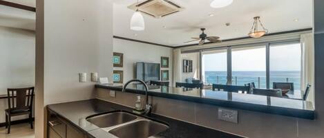 A modern kitchen with a large window overlooking the sea, a built-in sink, and pendant lighting.