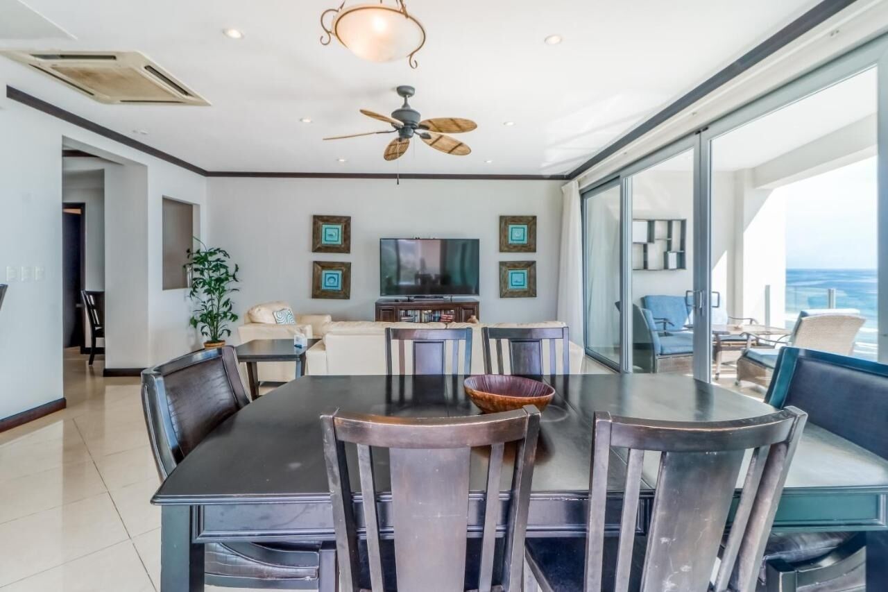 A modern dining area with a large table and chairs, a ceiling fan, and a television on the wall.