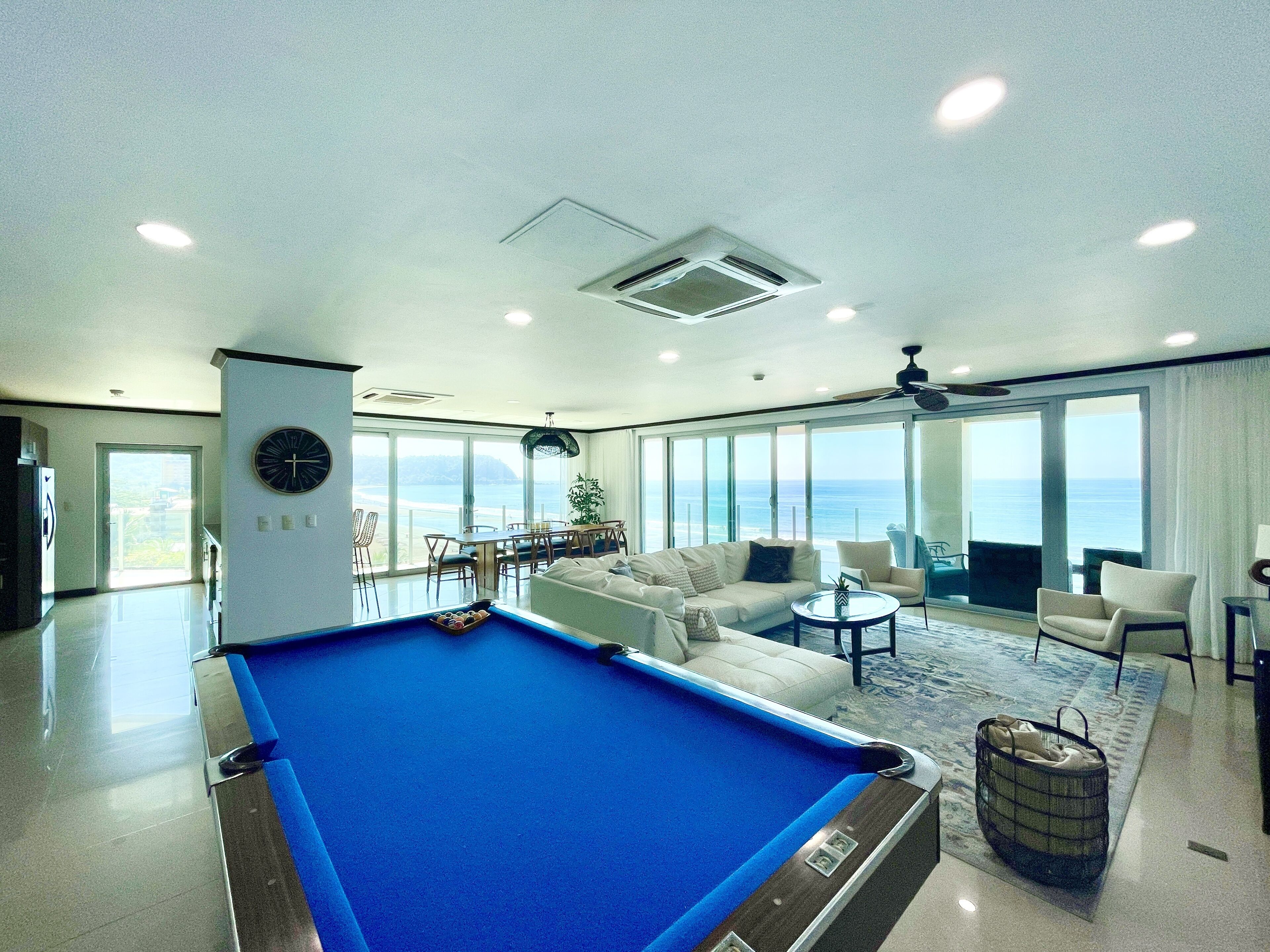 Un salon moderne avec une table de billard, un canapé et un coin repas offrant une vue sur l’océan.