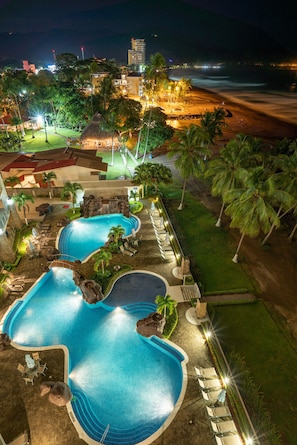 Een zwembadgedeelte van een resort met meerdere zwembaden, ligbedden en palmbomen.