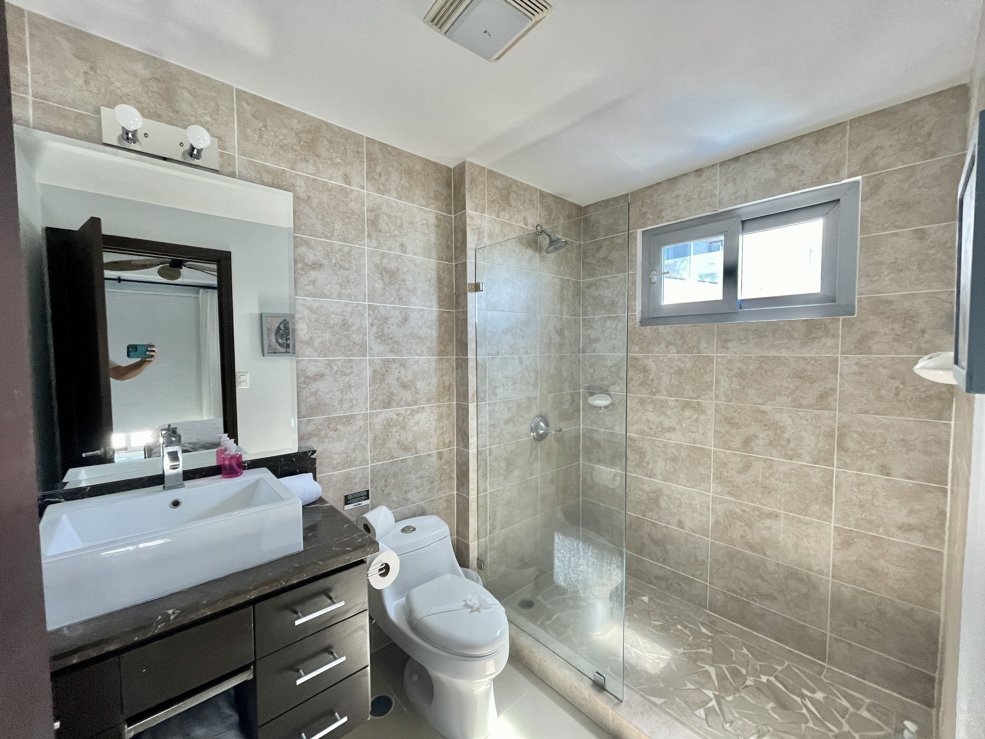 A modern bathroom with a glass-enclosed shower, a large mirror, and a vanity with a sink and countertop.