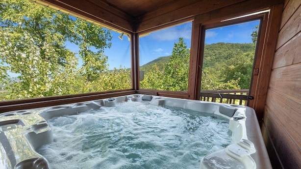 Un jacuzzi con terraza de madera y amplias ventanas con vistas a un bosque.