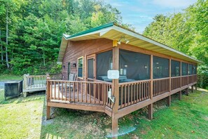 A wooden cabin with a covered deck, large windows, and a view of a forested area. - Little Little 2 Bedroom Cabin by RedAwning (Sevierville)