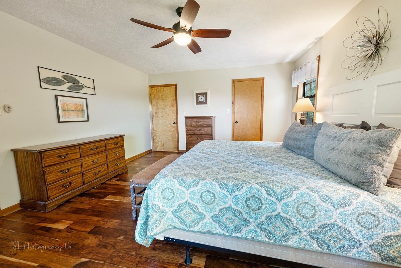A bedroom with a bed, wooden dresser, ceiling fan, and a fireplace.