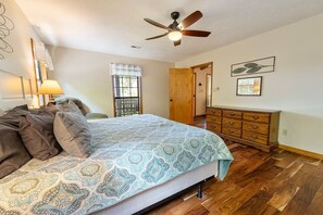 A bedroom with a bed, wooden dresser, ceiling fan, and a window with blinds. - Little Little 2 Bedroom Cabin by RedAwning (Sevierville)