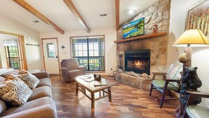 Una sala de estar acogedora con chimenea de piedra, piso de madera y un rincón de estar cómodo.