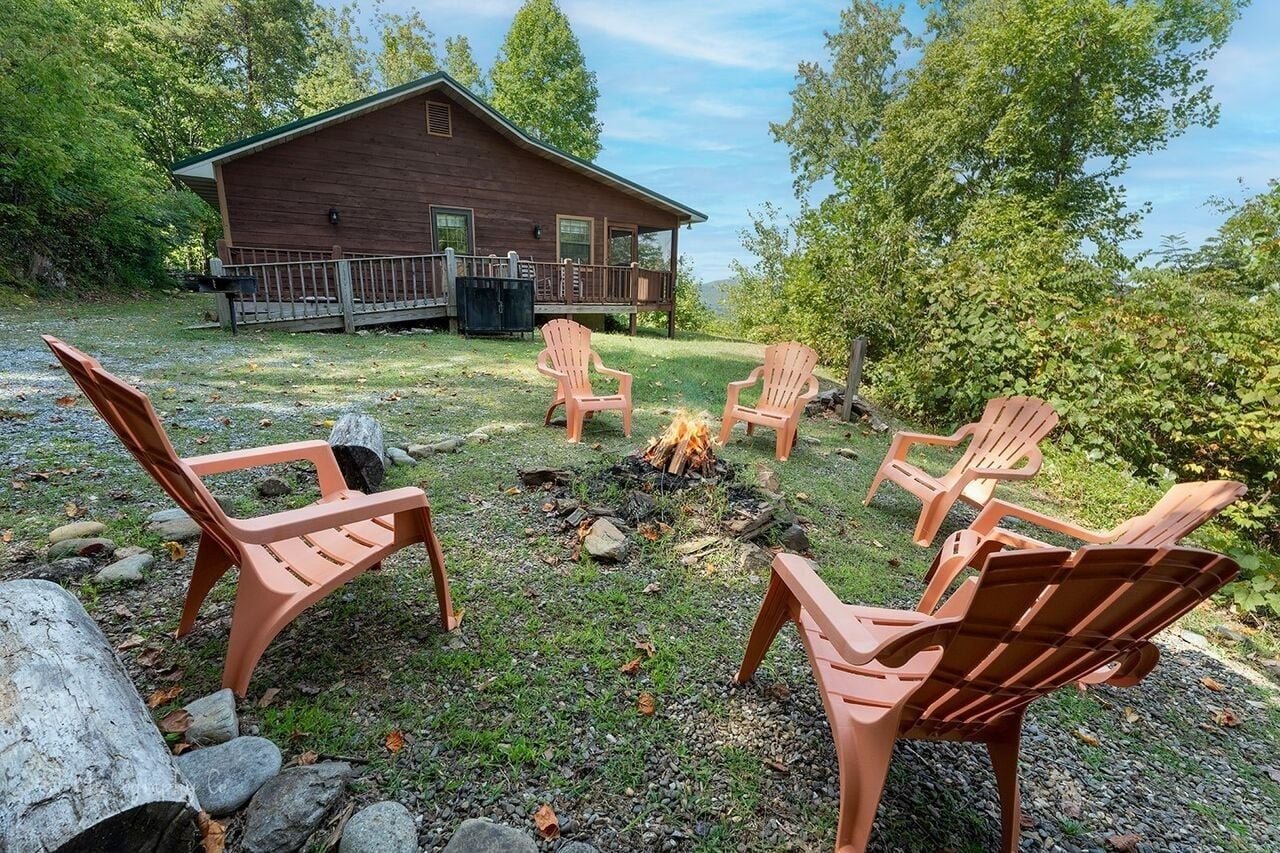 Une cabane dotée d’une terrasse, entourée d’un foyer et de chaises d’extérieur.